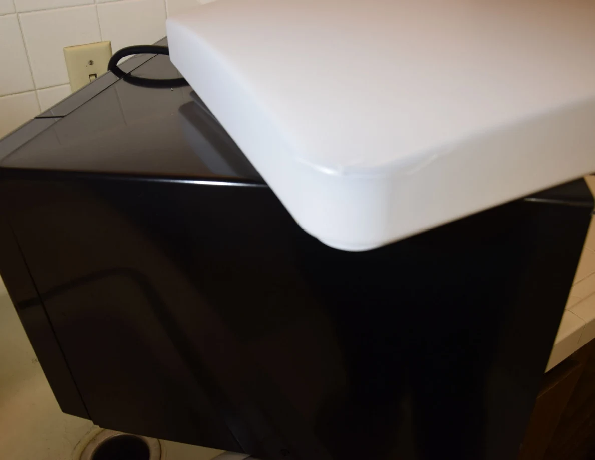 Close view of a white light cover resting on a black countertop appliance.