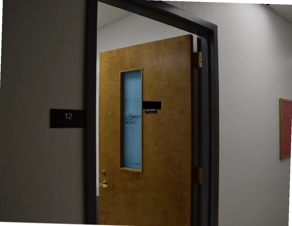 Open wooden office door with narrow wired-glass window, room number 12 and a blacked-out label.