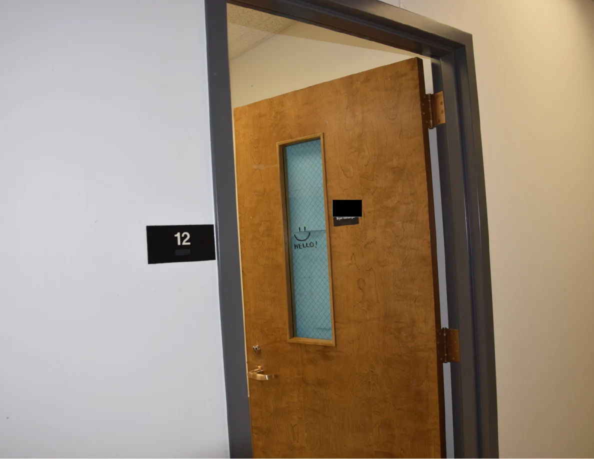 Office doorway with room number 12, wooden door and partly redacted nameplate.