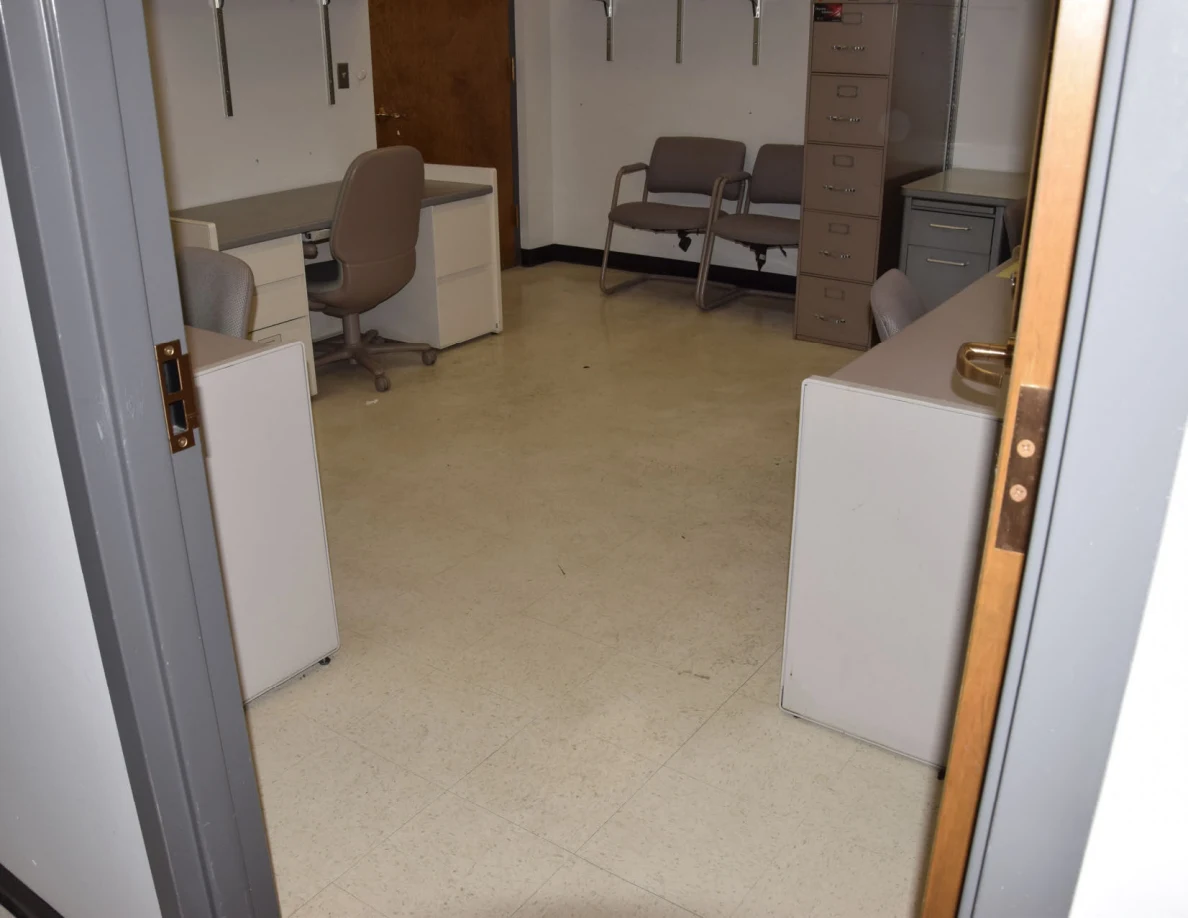 Office entrance showing desks, chairs and a tall filing cabinet.
