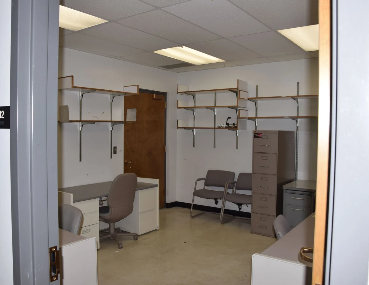 Office with desks, chairs, filing cabinets and mostly empty wall shelves.