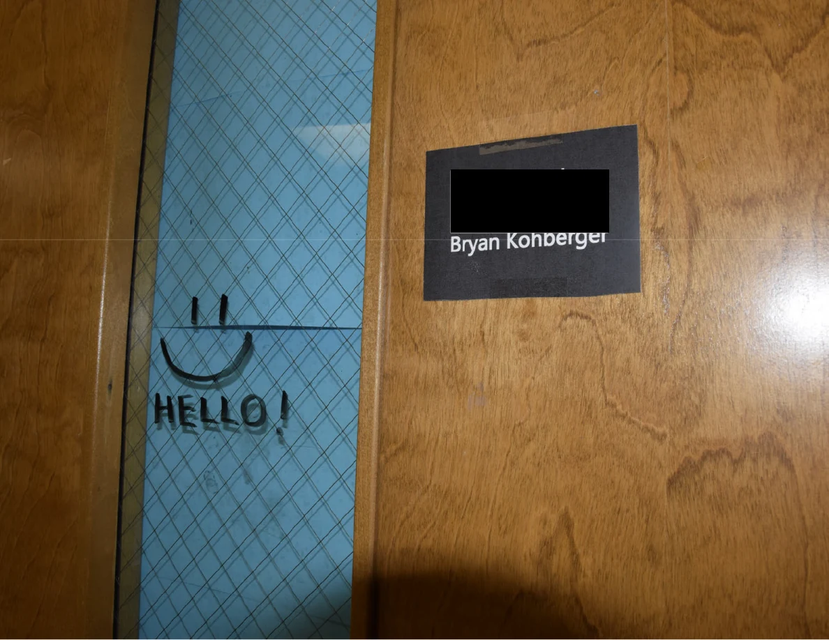 Close view of wooden office door with a narrow glass window, drawn smiley face and partly redacted nameplate.