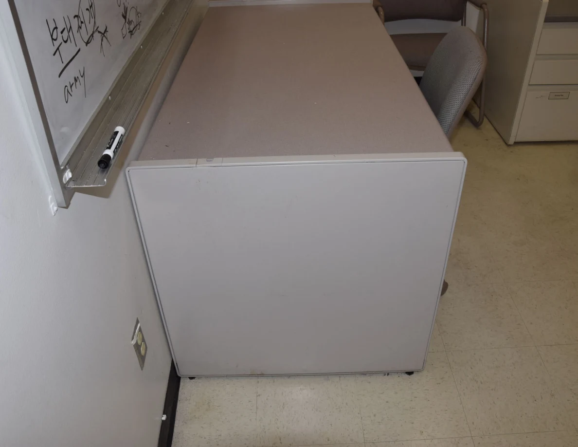 Office desk below a whiteboard with handwriting and a marker on its tray.