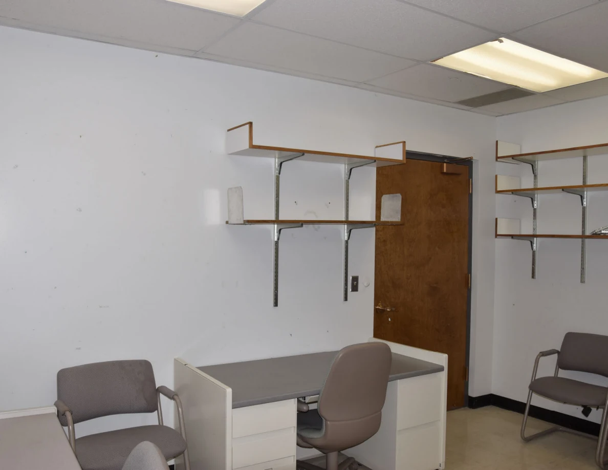 Office desk and chairs beneath mostly empty wall shelves.