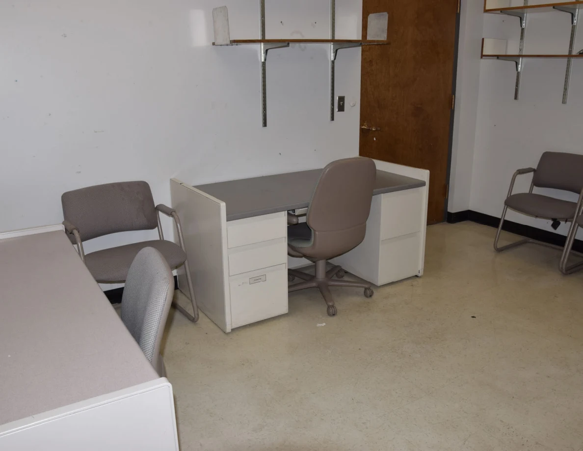 Office desks and upholstered chairs on pale floor tiles.