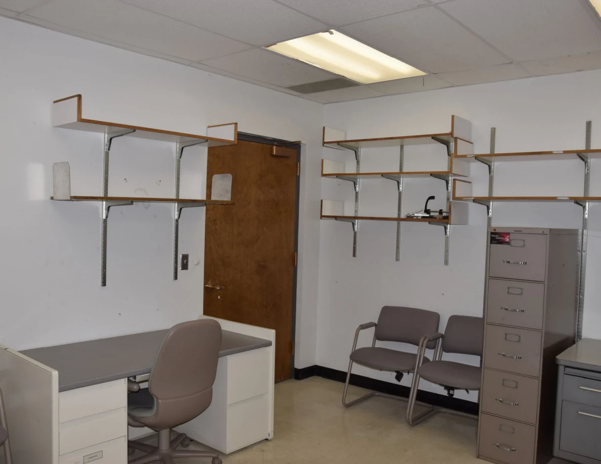 Wall shelves above an office desk, chairs and tall filing cabinet.