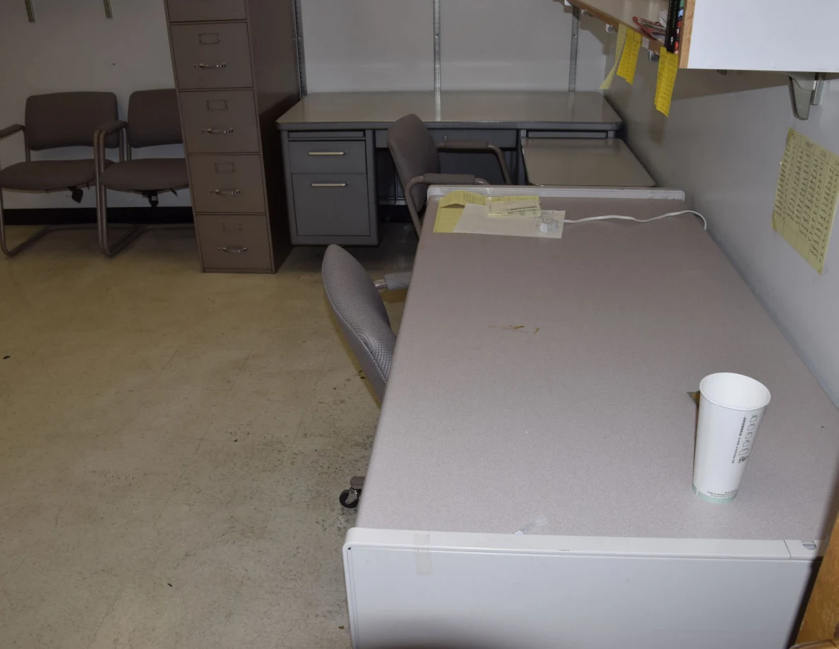 Office desk with a white cup and telephone, with chairs and filing cabinets behind.