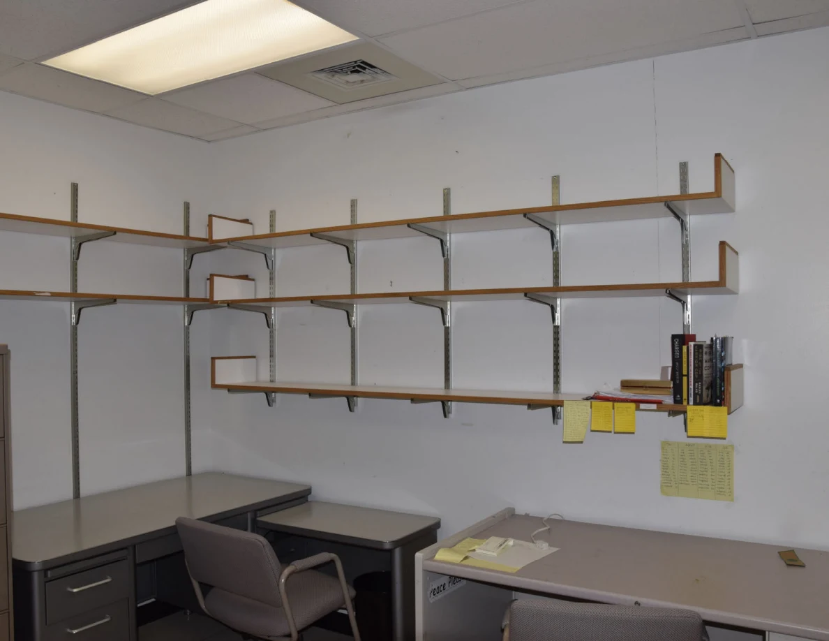 Mostly empty office wall shelves above desks, with a few books and yellow notes.