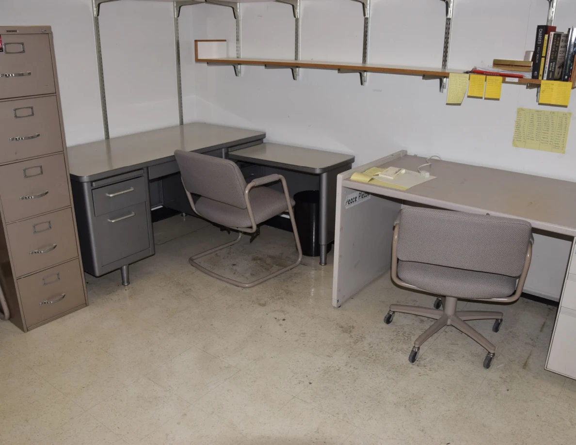 Two office desks and chairs beside a tall filing cabinet.