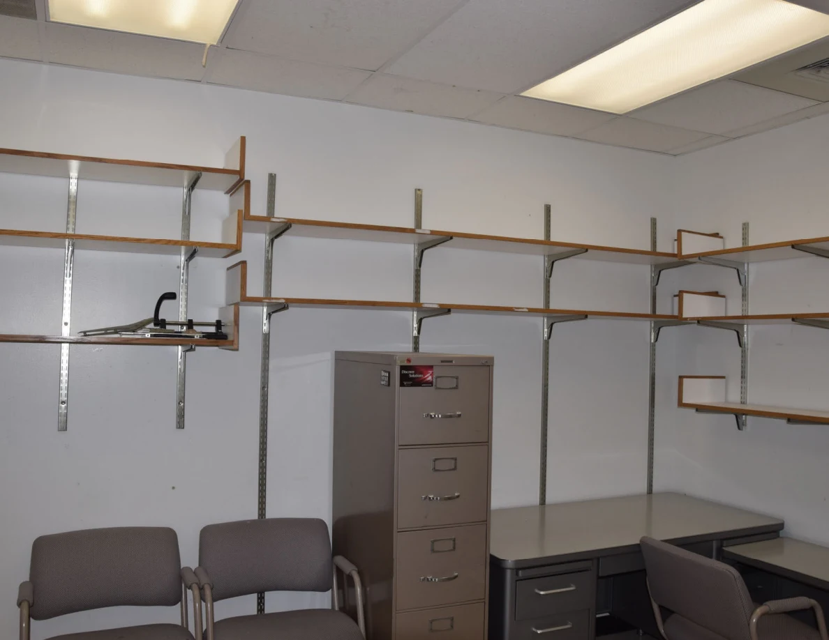 Office wall shelves above visitor chairs, filing cabinet and corner desk.
