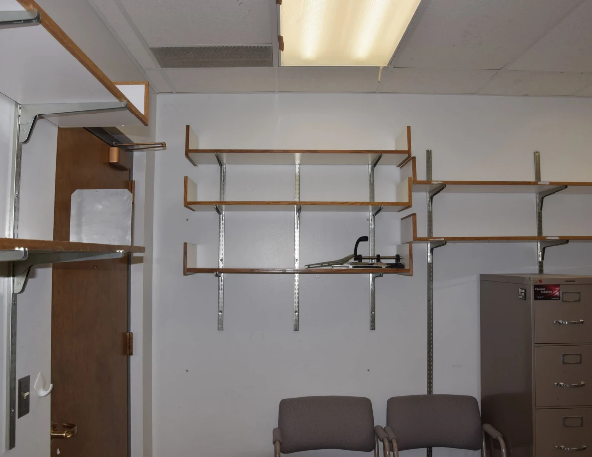Upper office shelves and ceiling light above chairs and a wooden door.