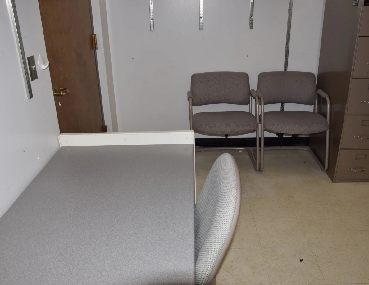 Office desk in foreground with two visitor chairs against the far wall.