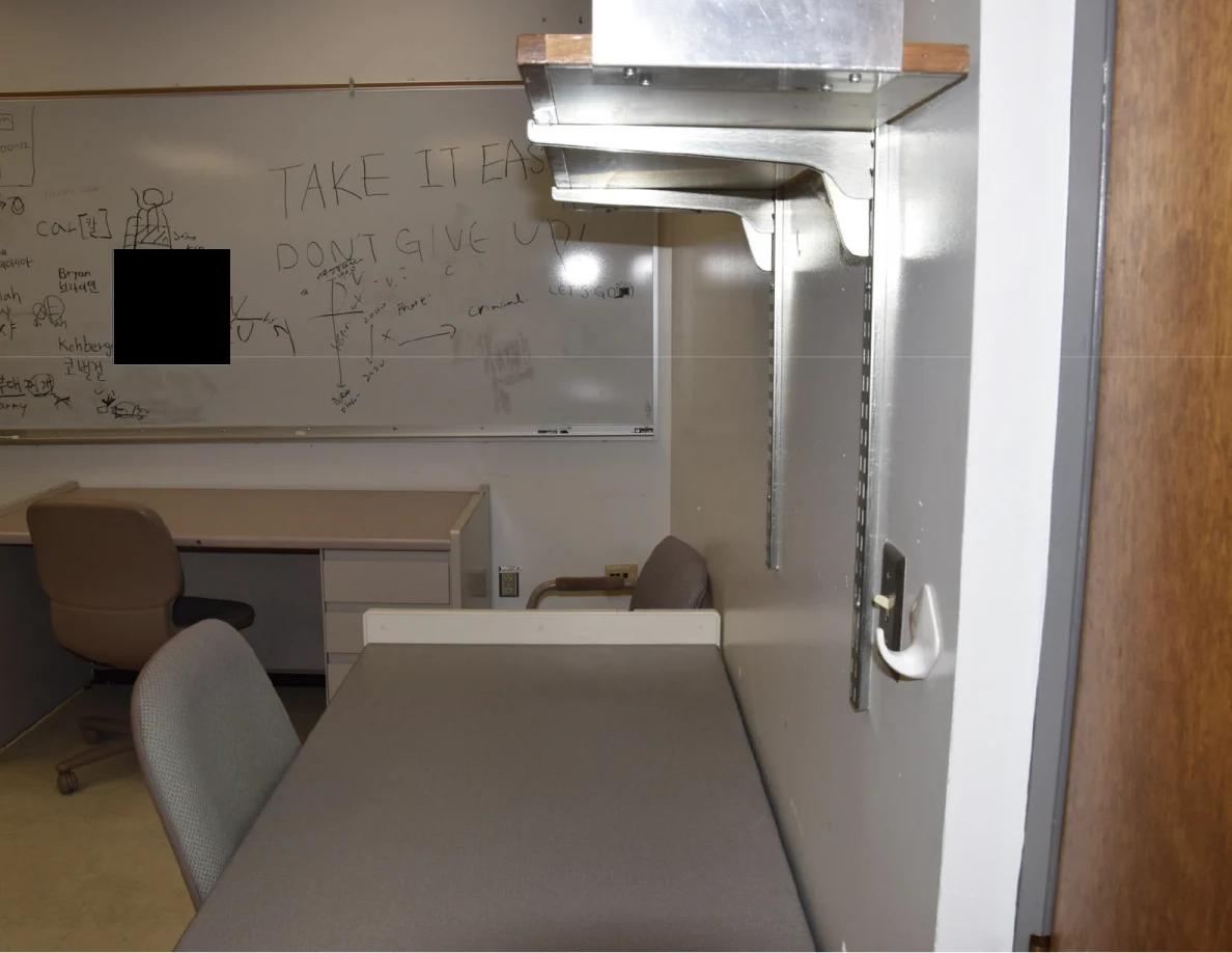 Office desks below a whiteboard with handwritten messages and a black redaction.
