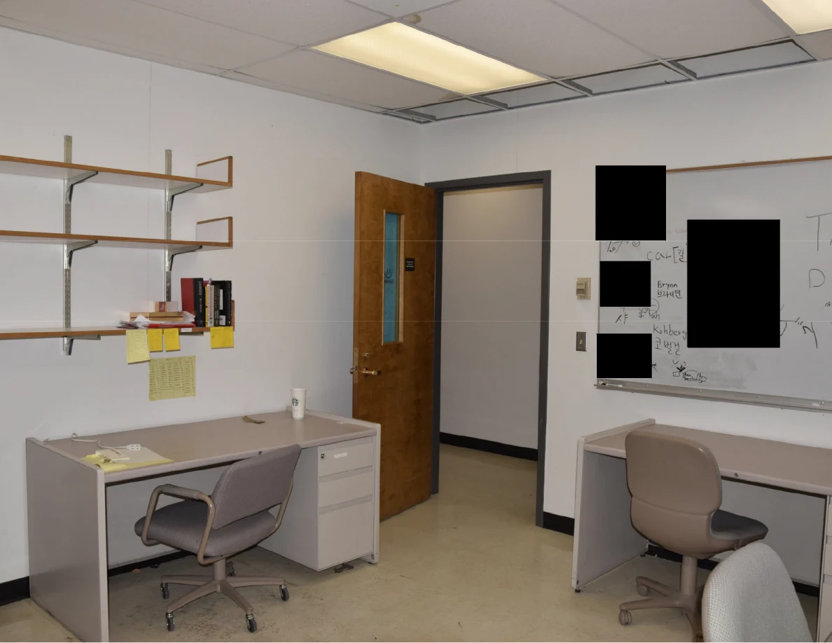 Office desks, wall shelves and partly redacted whiteboard beside an open door.