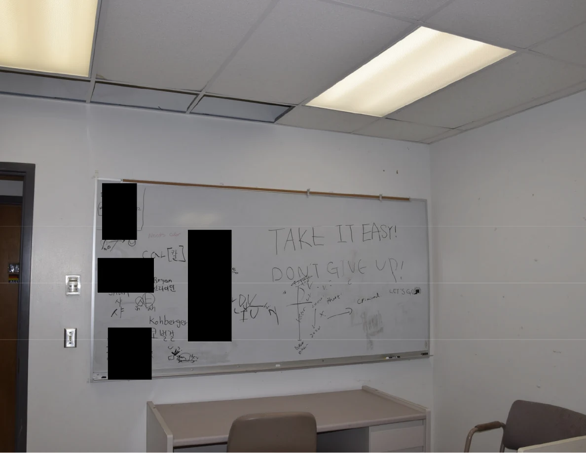 Whiteboard with handwritten messages and black redactions beneath fluorescent ceiling lights.