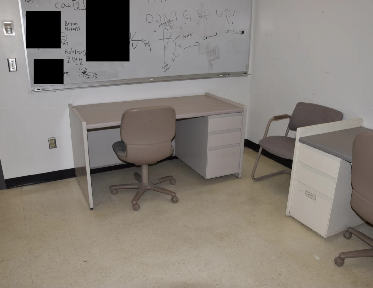 Desk and rolling chair below a partly redacted whiteboard.