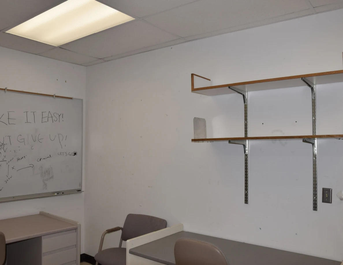 Empty office wall shelves beside a whiteboard and visitor chair.