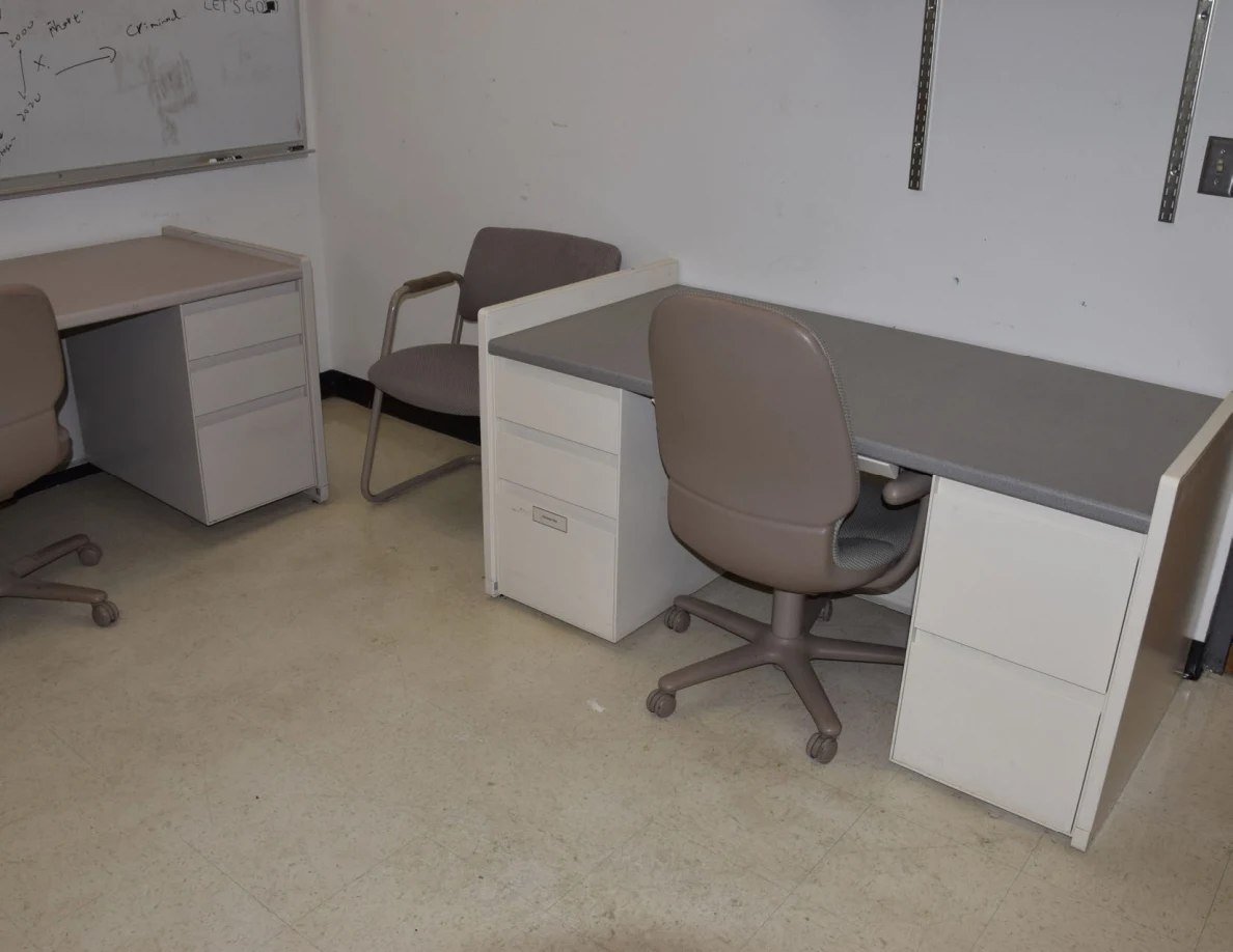 Office desk with drawers and a rolling chair beneath empty shelves.