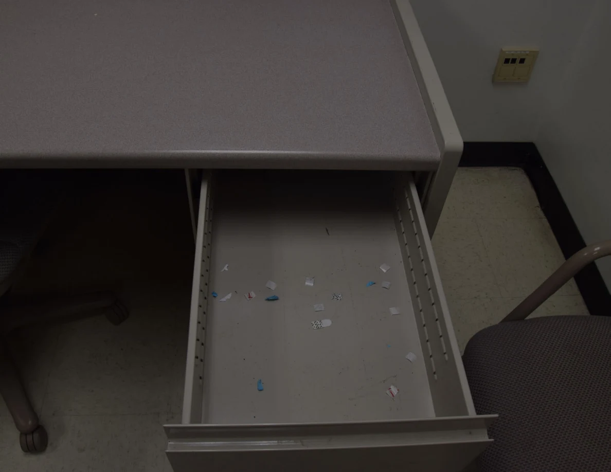 Open desk drawer containing scattered tiny paper scraps.
