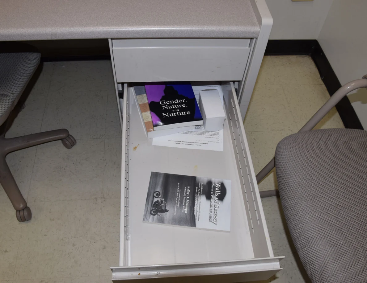 Open desk drawer with books, a booklet and loose papers.