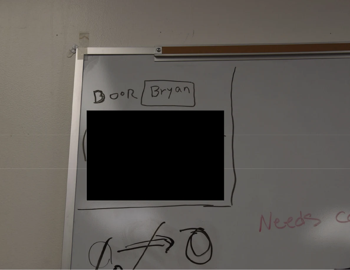 Close view of a whiteboard corner with a handwritten label and large black redaction.