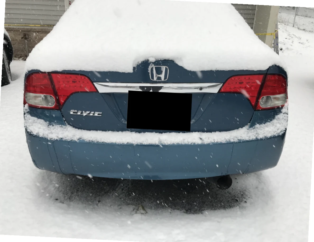 Rear of a blue Honda Civic covered in snow, with license plate blacked out.
