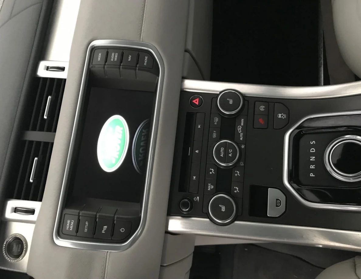 Vehicle center console with Land Rover logo on screen, climate controls and rotary gear selector.