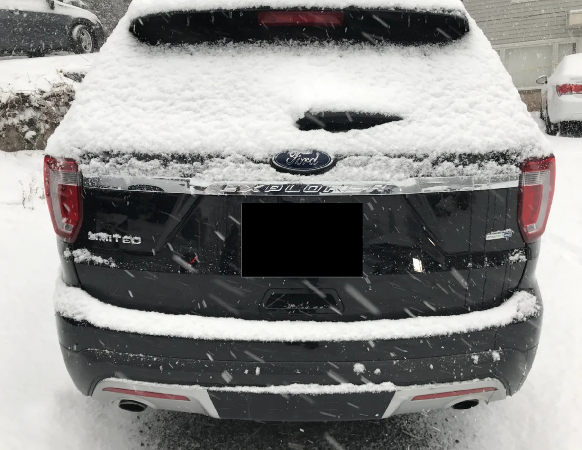 Snow-covered rear of a dark Ford Explorer with license plate blacked out.