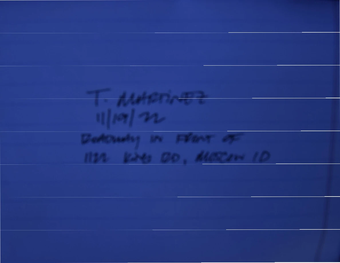 Blue-tinted photograph of lined paper with a handwritten name, date and roadway location note.