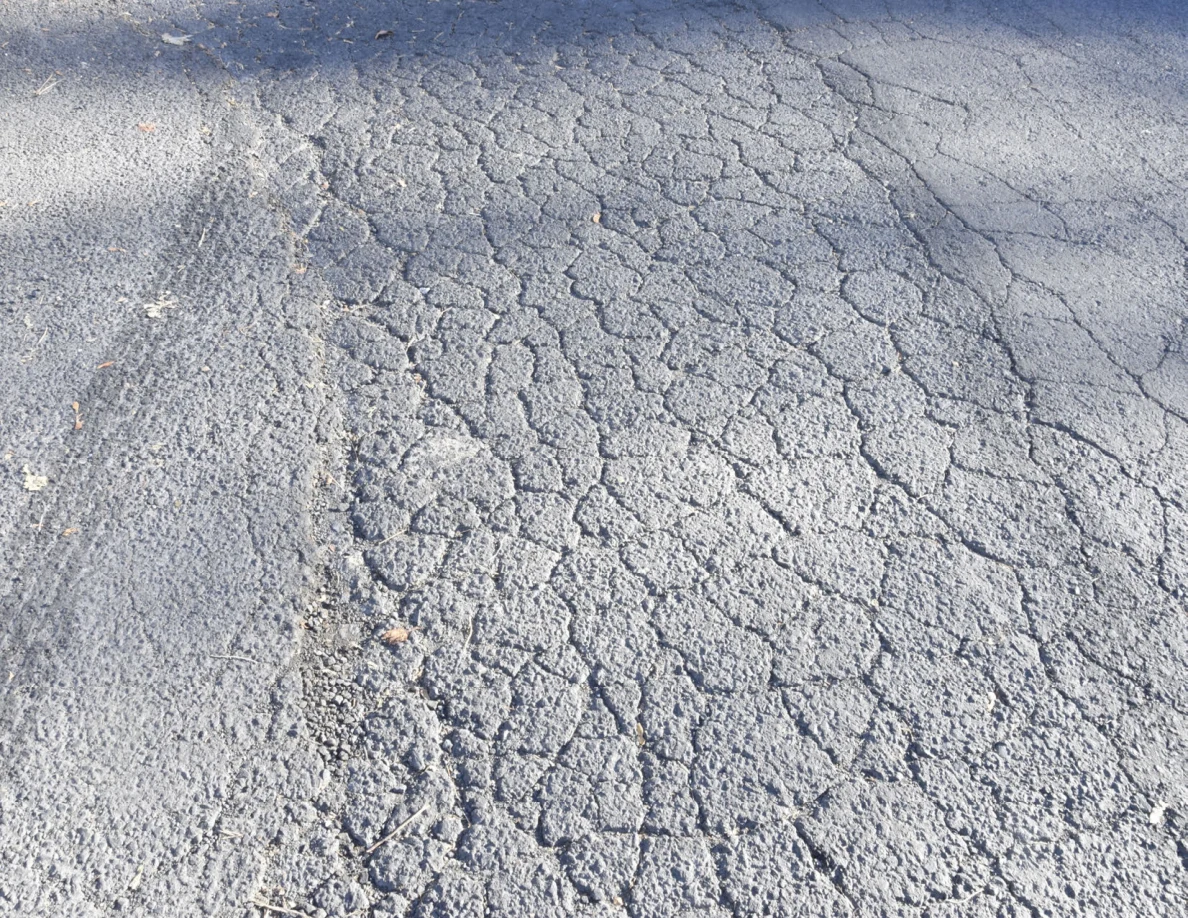 Close view of cracked asphalt with darker curved marks across its surface.