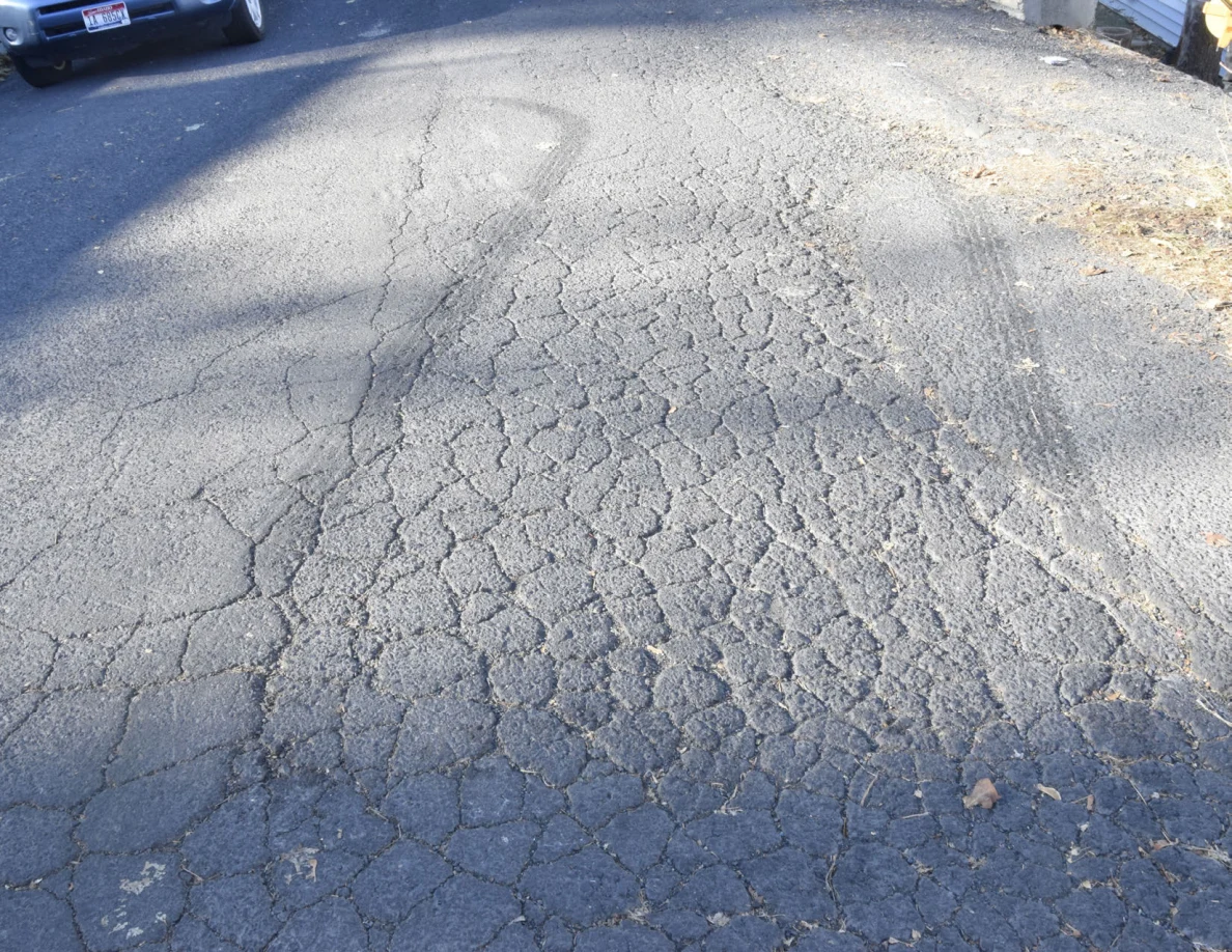 Cracked roadway with a broad curved dark mark and part of a parked vehicle.