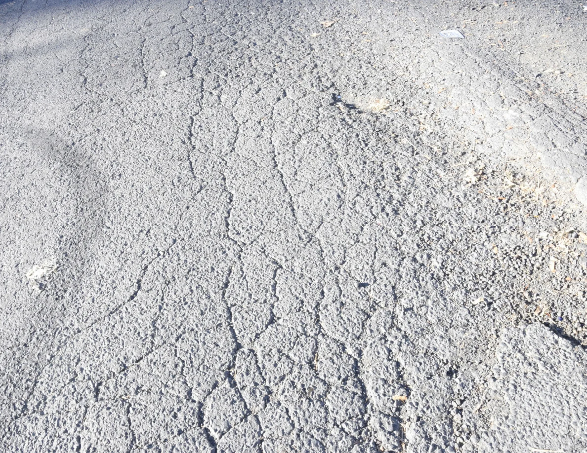 Close view of asphalt cracks and a broad darker mark near a road edge.