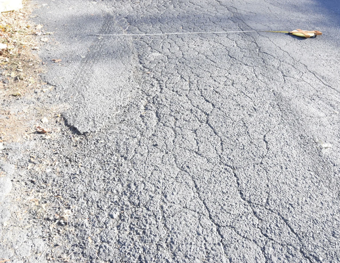 Measuring tape stretched across cracked roadway beside its case.