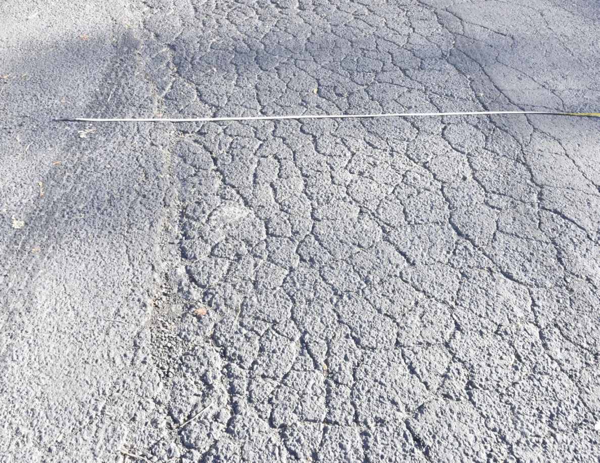 Measuring tape crossing cracked asphalt and dark surface marks.