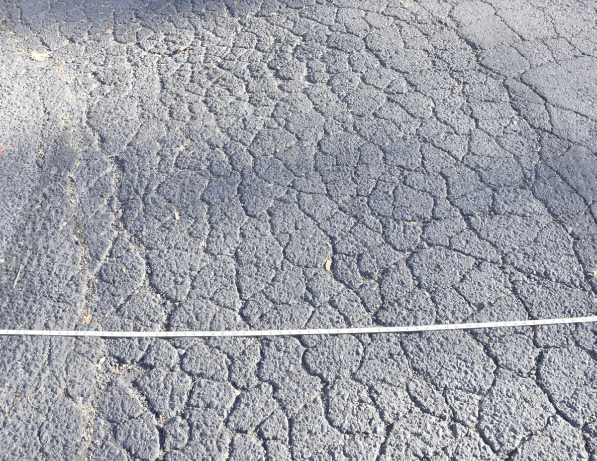 Roadway cracks and dark bands above a stretched measuring tape.