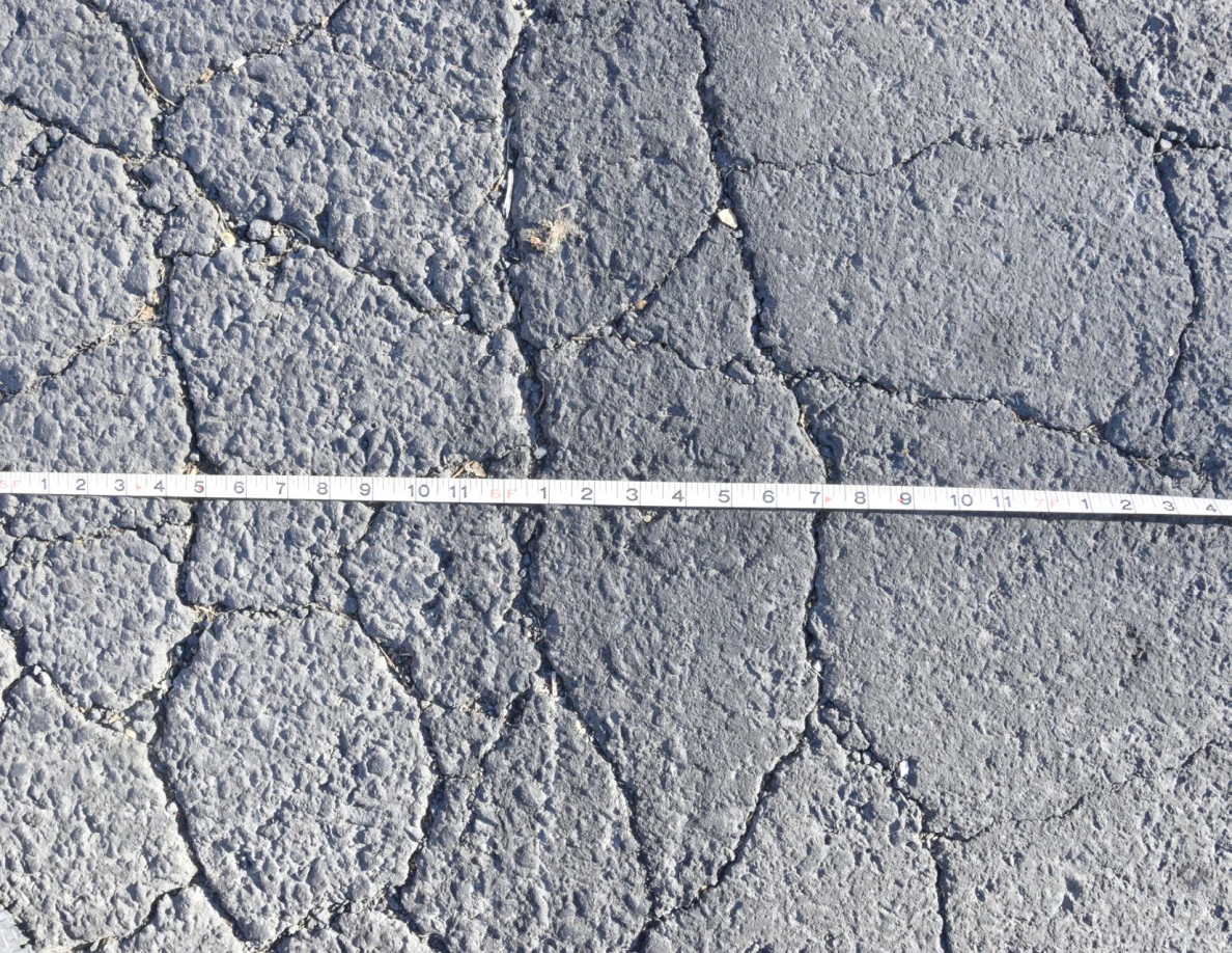 Measuring tape across branching cracks in asphalt.