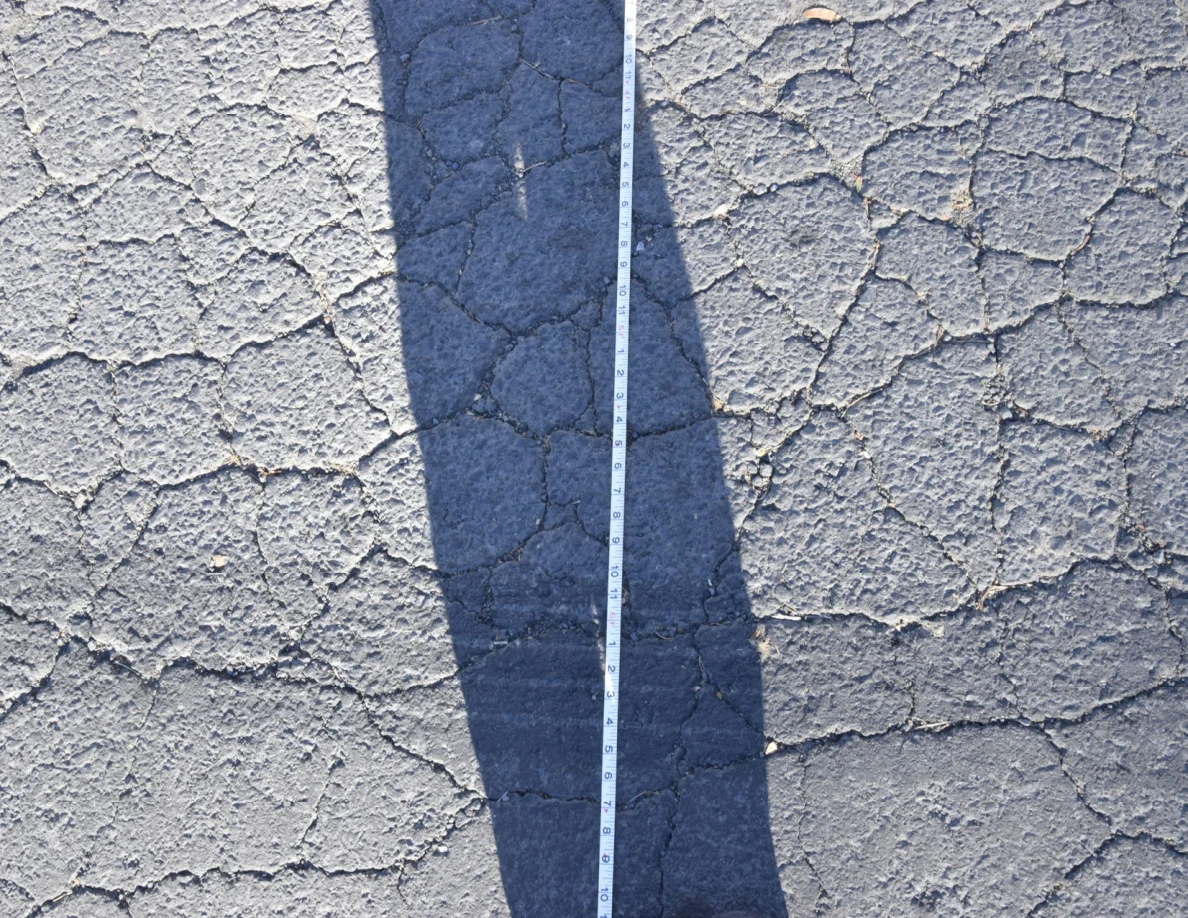 Long measuring tape laid along cracked pavement through a person's shadow.