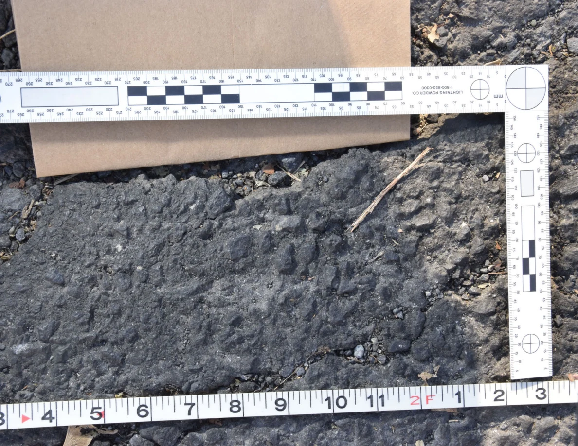 L-shaped photographic scale and measuring tape surrounding a rough asphalt patch.