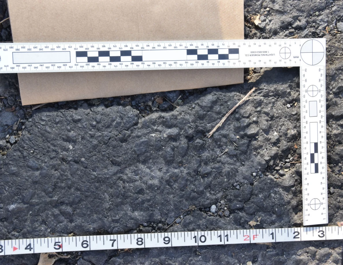 Rough roadway patch beneath a brown envelope, framed by measurement scales.
