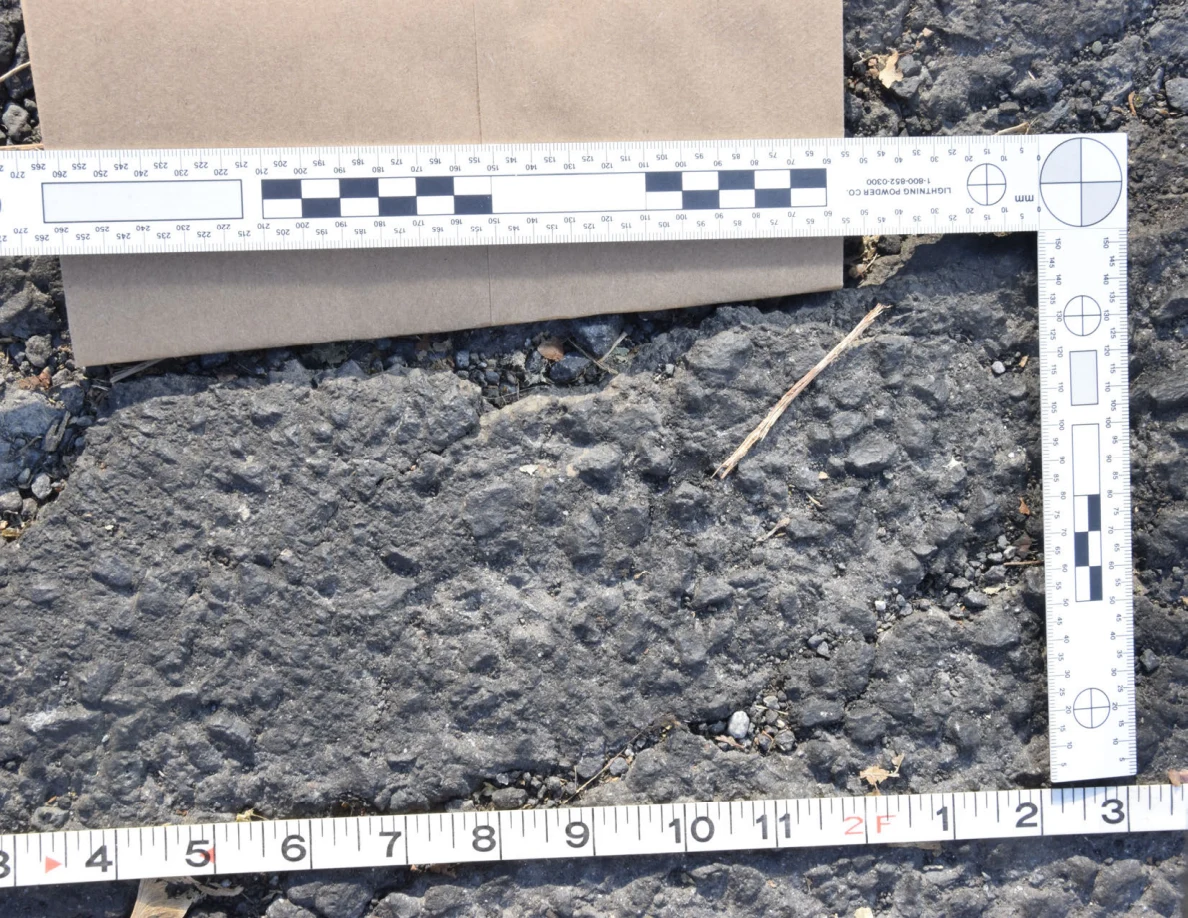 Close view of uneven asphalt within an L-shaped scale and tape measure.