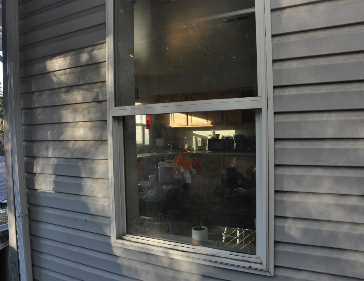 Angled view of an exterior window, with a kitchen counter and cabinets visible through the glass.