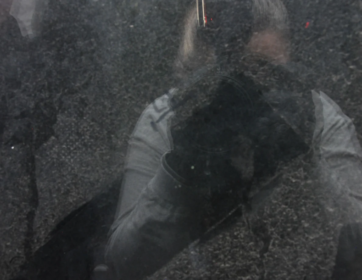 Close view of dark window glass reflecting a person holding a camera.