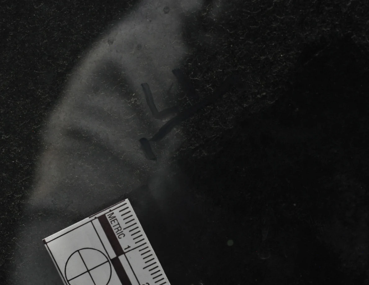 Dark window-glass close-up with an arrow-shaped mark and a corner of a metric scale.