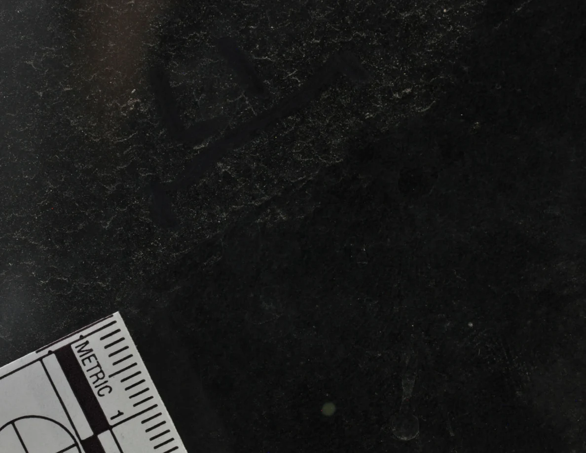 Dark reflective glass with an arrow-shaped mark and a corner of a metric scale.