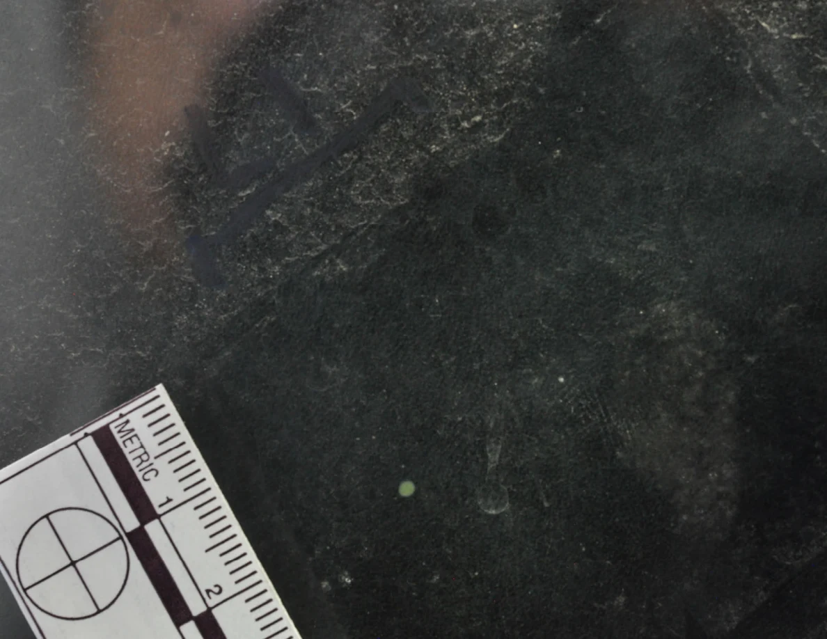 Dark glass close-up with reflected light, an arrow-shaped marker and a metric scale.
