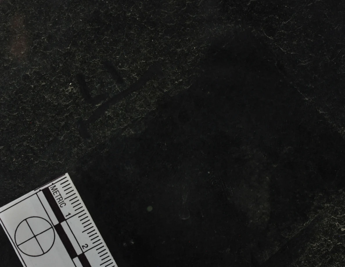 Dark glass close-up with reflected light, an arrow-shaped marker and a metric scale.