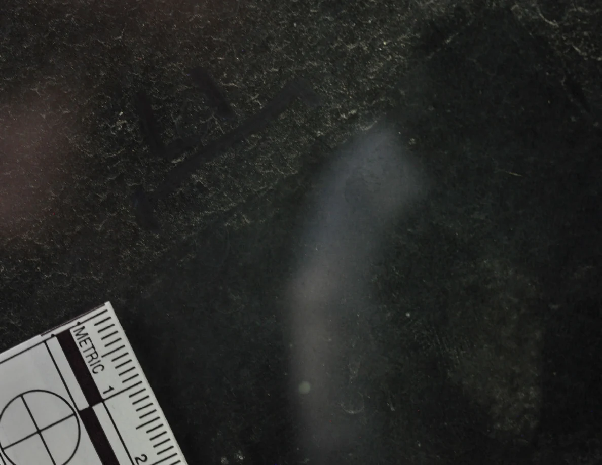 Dark glass close-up with reflected light, an arrow-shaped marker and a metric scale.