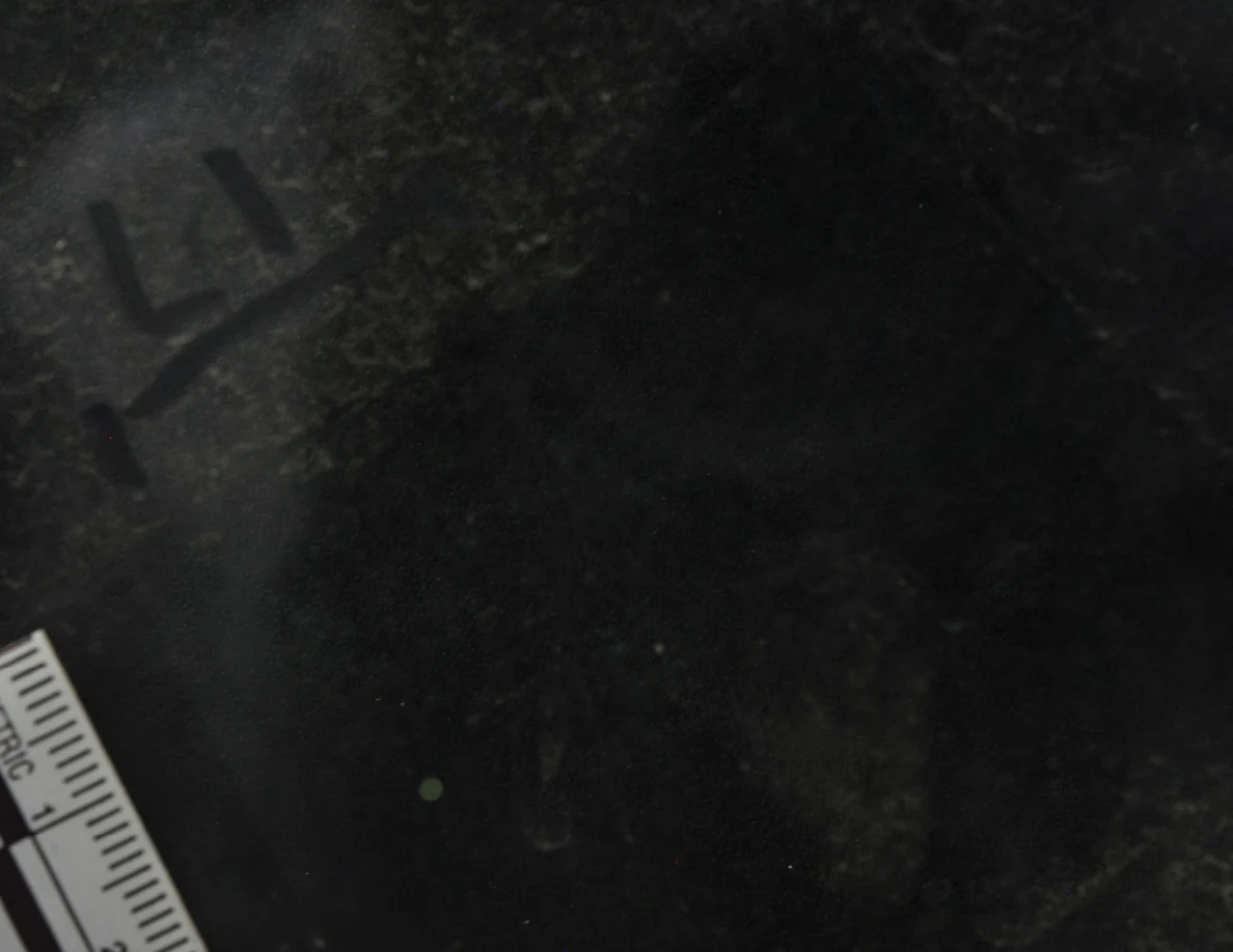 Dark glass close-up with reflected light, an arrow-shaped marker and a metric scale.