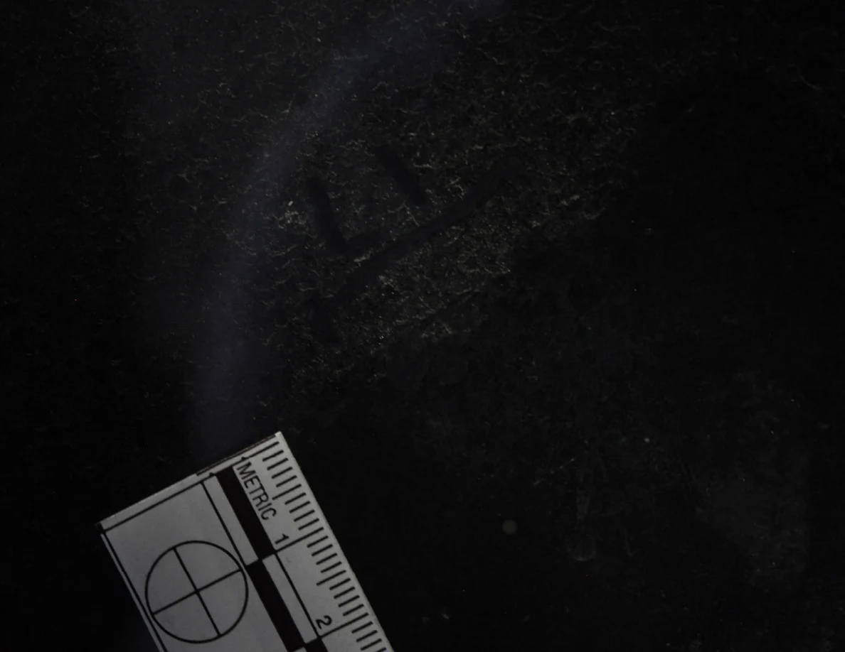 Dark glass close-up with reflected light, an arrow-shaped marker and a metric scale.