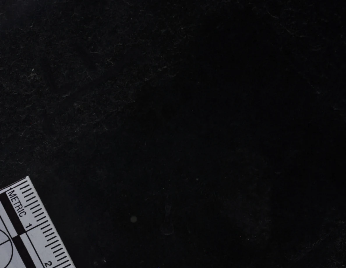 Dark glass close-up with reflected light, an arrow-shaped marker and a metric scale.